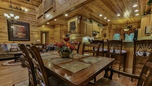 A wooden interior with a dining table, chairs, a sofa, and a kitchen area.