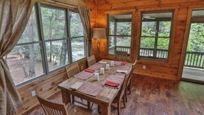 Eine Holzdiele mit Esstisch, gedeckt für sechs Personen, großen Fenstern und Blick ins Waldgebiet.