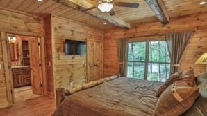 Ein Schlafzimmer einer Holzhütte mit einem Bett, einem Deckenventilator und einem Fenster mit Vorhängen.