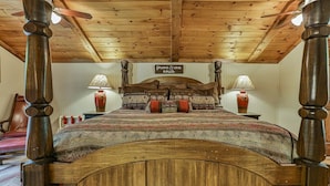A wooden bed with a headboard, two bedside lamps, and a sign above the bed. - Rendezvous on the River | Ellijay, GA (Ellijay)