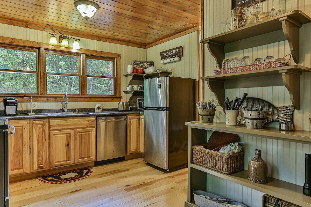 A kitchen with wooden cabinets, a stainless steel refrigerator, and a window with a view of trees.