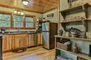 Una cocina con armarios de madera, un refrigerador de acero inoxidable y una ventana con vistas a árboles.