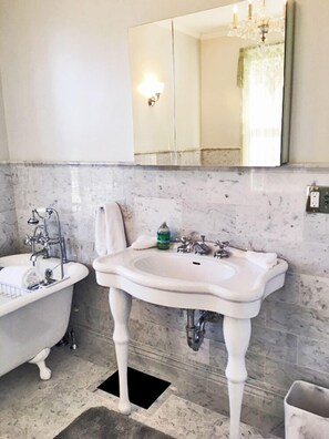 A bathroom with a clawfoot bathtub, a pedestal sink, and a large mirror. - Victorian Seasons Stirling (Greenport)