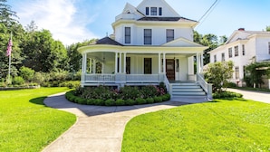 A two-story house with a wrap-around porch, a front entrance with steps, and a flagpole.