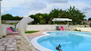 A swimming pool with a decorative stone sculpture, lounge chairs, and a covered area. - Aux Orangers (Luxe)