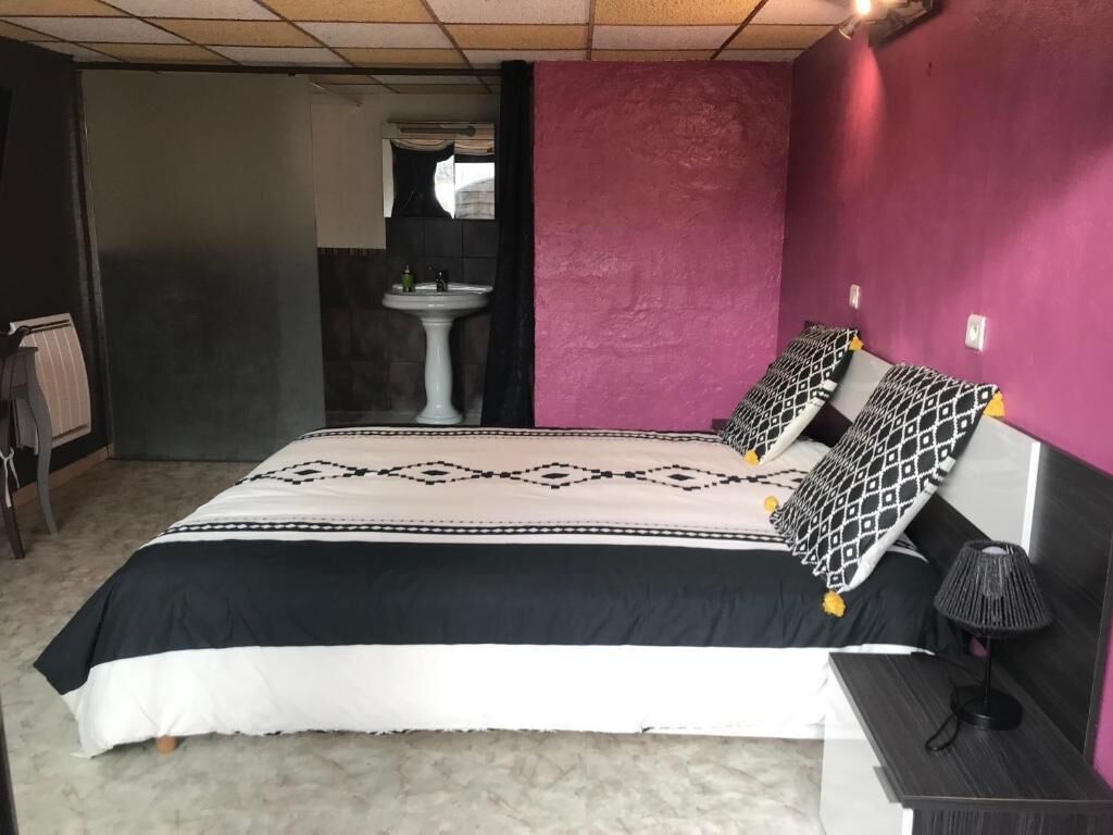 A bedroom with a bed, a nightstand, a lamp, and a bathroom visible in the background.