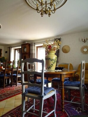A dining area with a chandelier, a large vase with flowers, and a patterned rug. - Aux Orangers (Luxe)