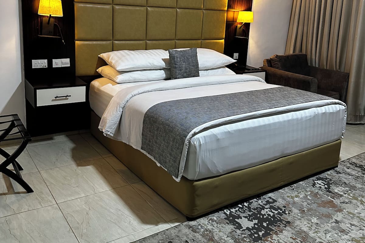 Habitación de hotel moderna con una cama grande, dos mesitas de noche, una butaca y una alfombra estampada.