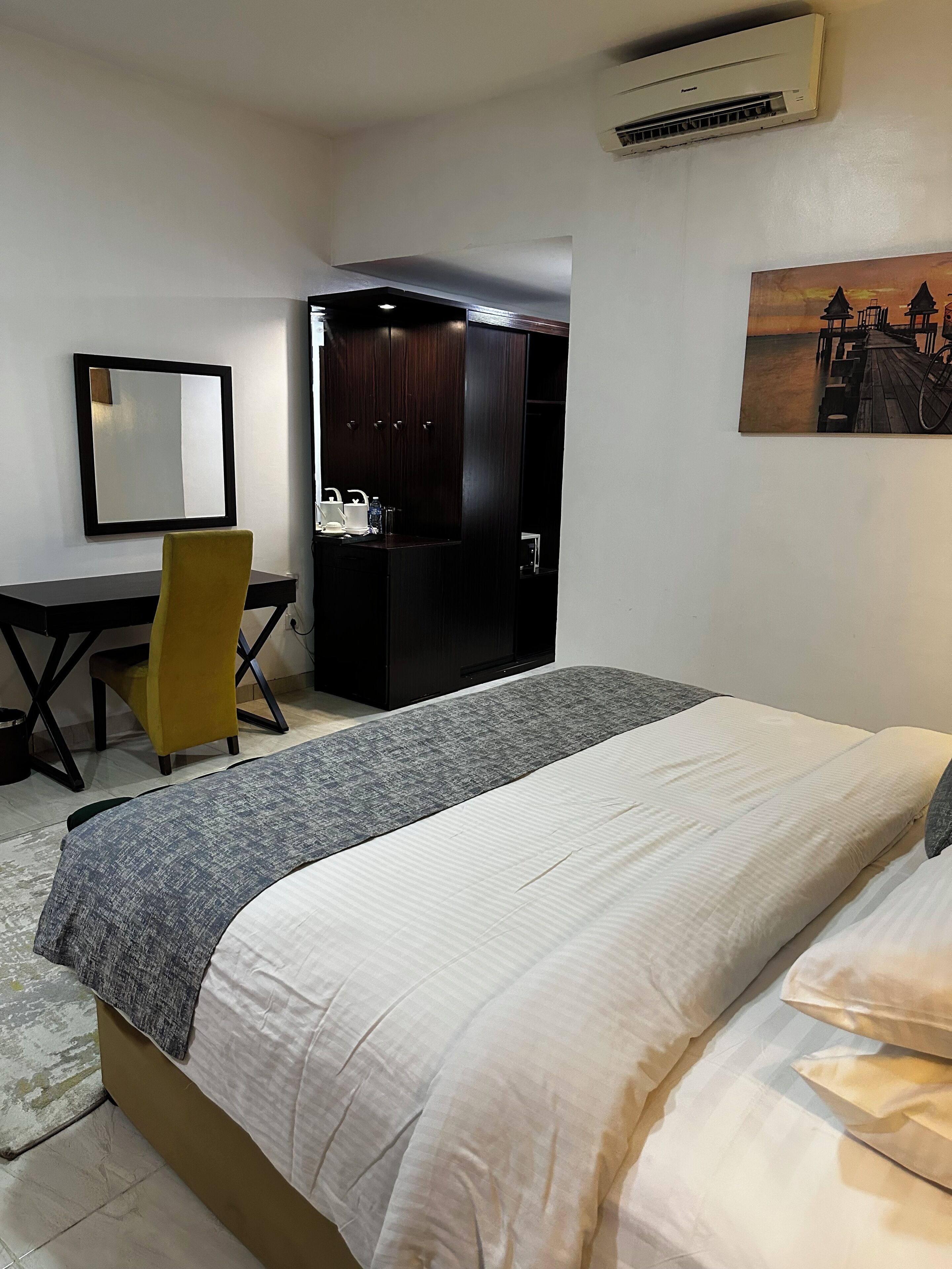 Een hotelkamer met een bed, bureau, stoel, kledingkast en een schilderij aan de muur.