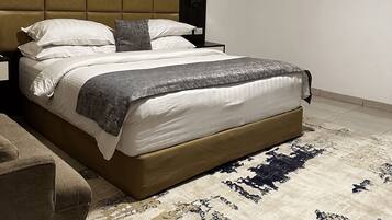 A modern hotel room with a large bed, a headboard, a nightstand, a lamp, and a painting on the wall.