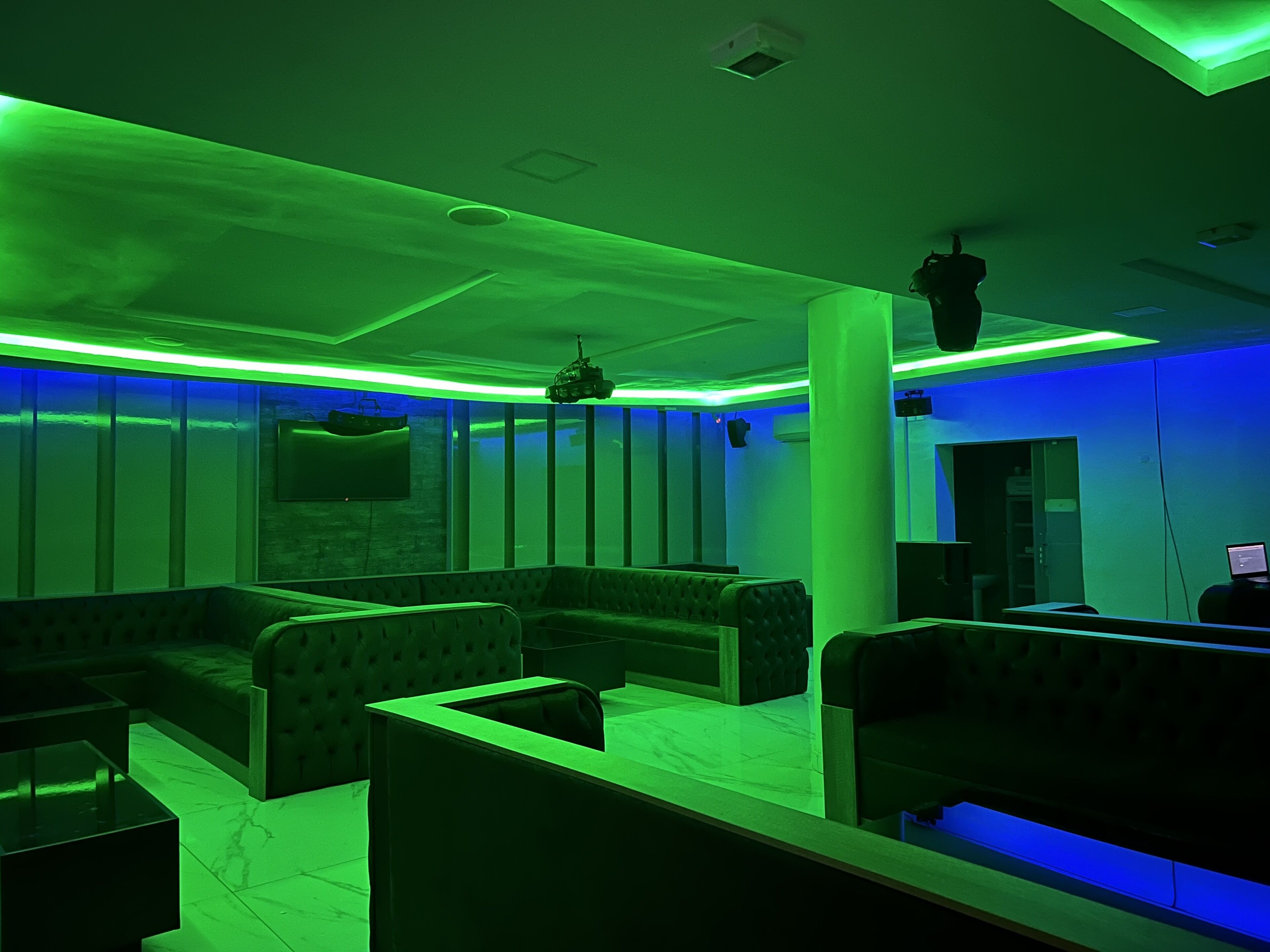 A room with green ambient lighting, a large column, and a seating area with a sofa and a table.