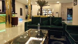 Un vestíbulo moderno con un sofá verde, una mesa de centro de vidrio y un árbol de palma como elemento central.