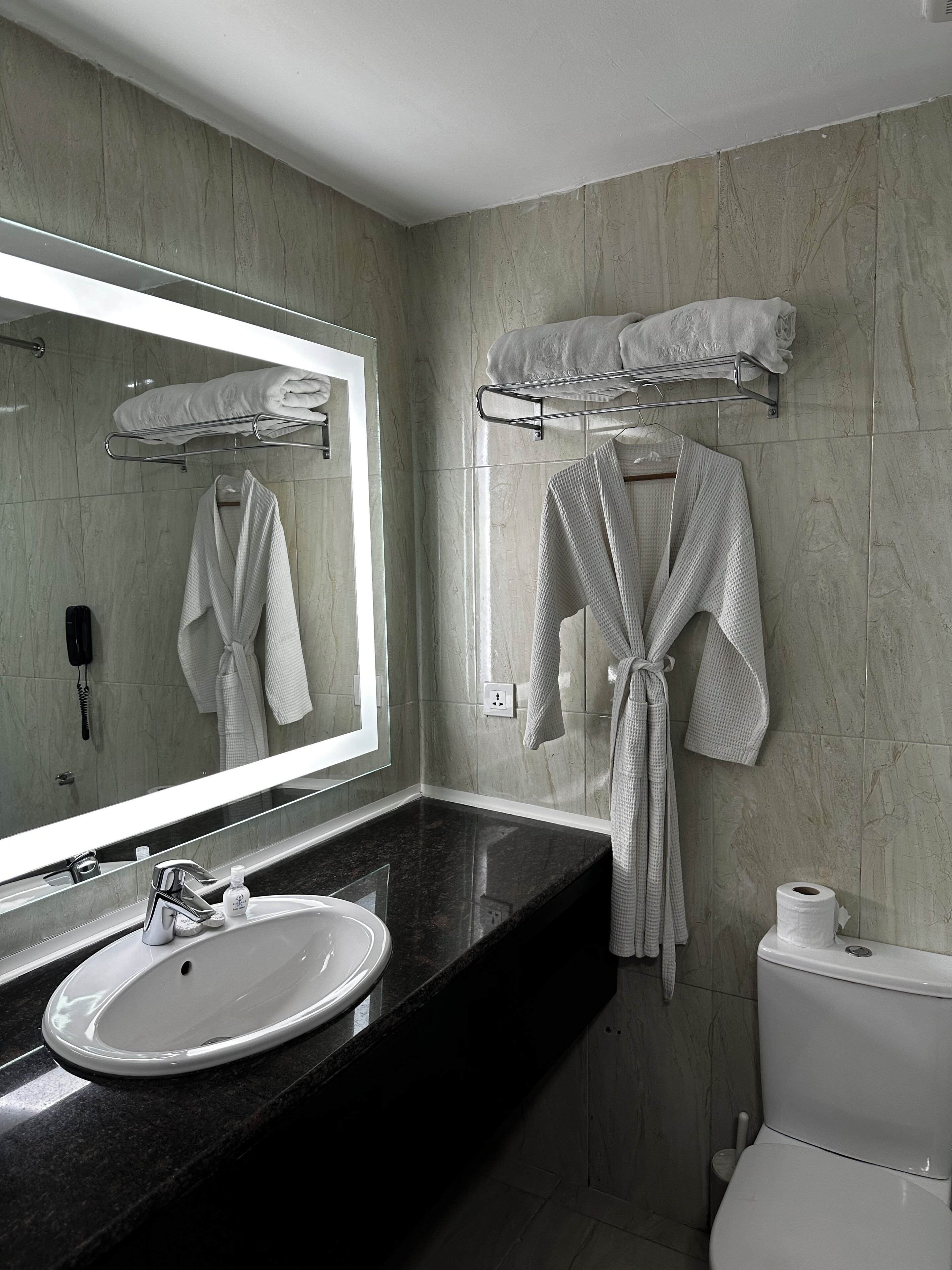 Een badkamer met een wastafel, spiegel, handdoekhouder en toilet.
