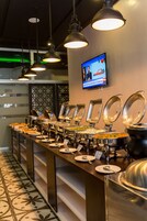 A buffet setup with multiple serving stations, a television mounted on the wall, and patterned floor tiles.