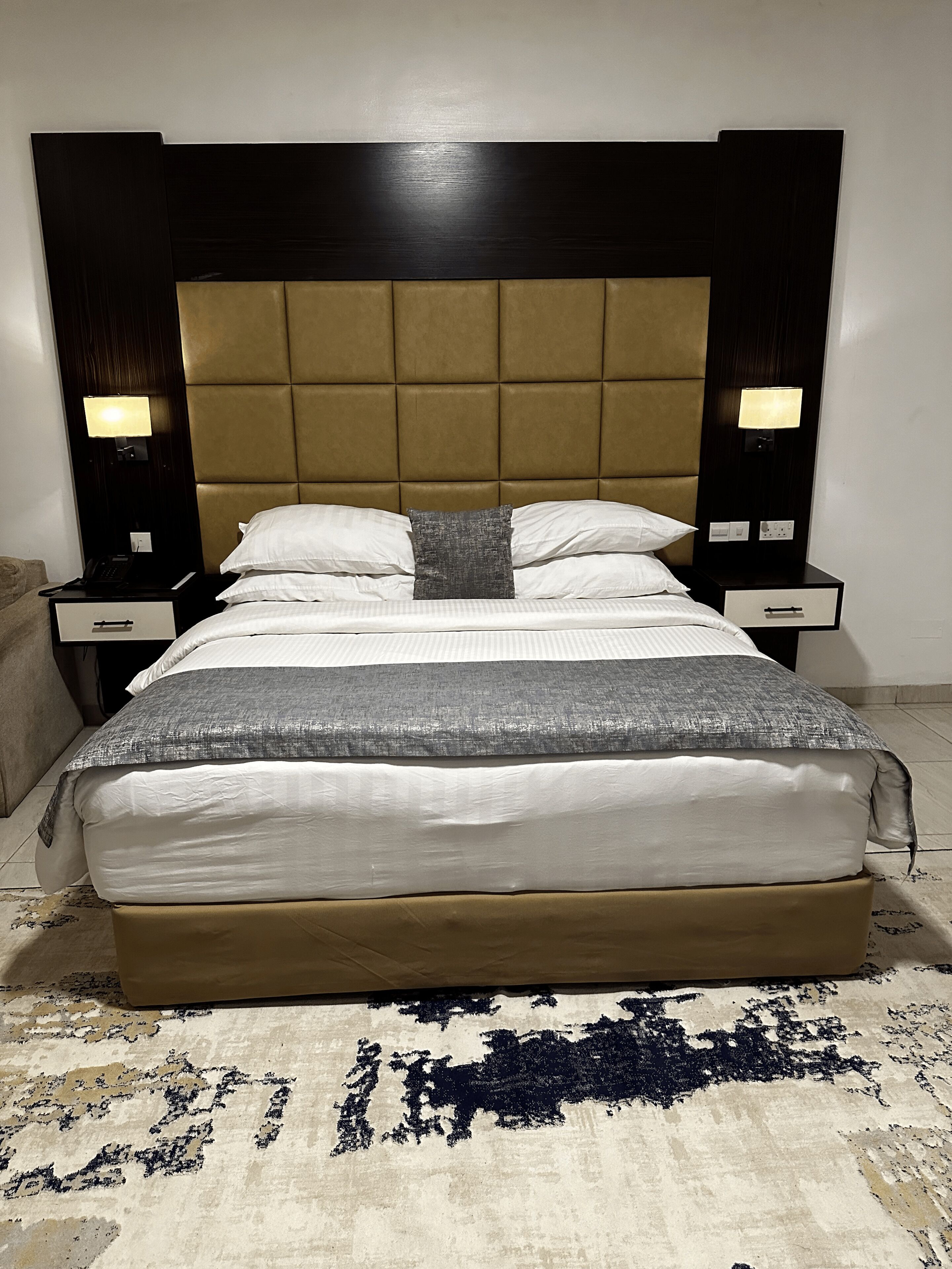 Een bed met hoofdbord, twee nachtkastjes, een klein tafeltje en een vloerkleed.
