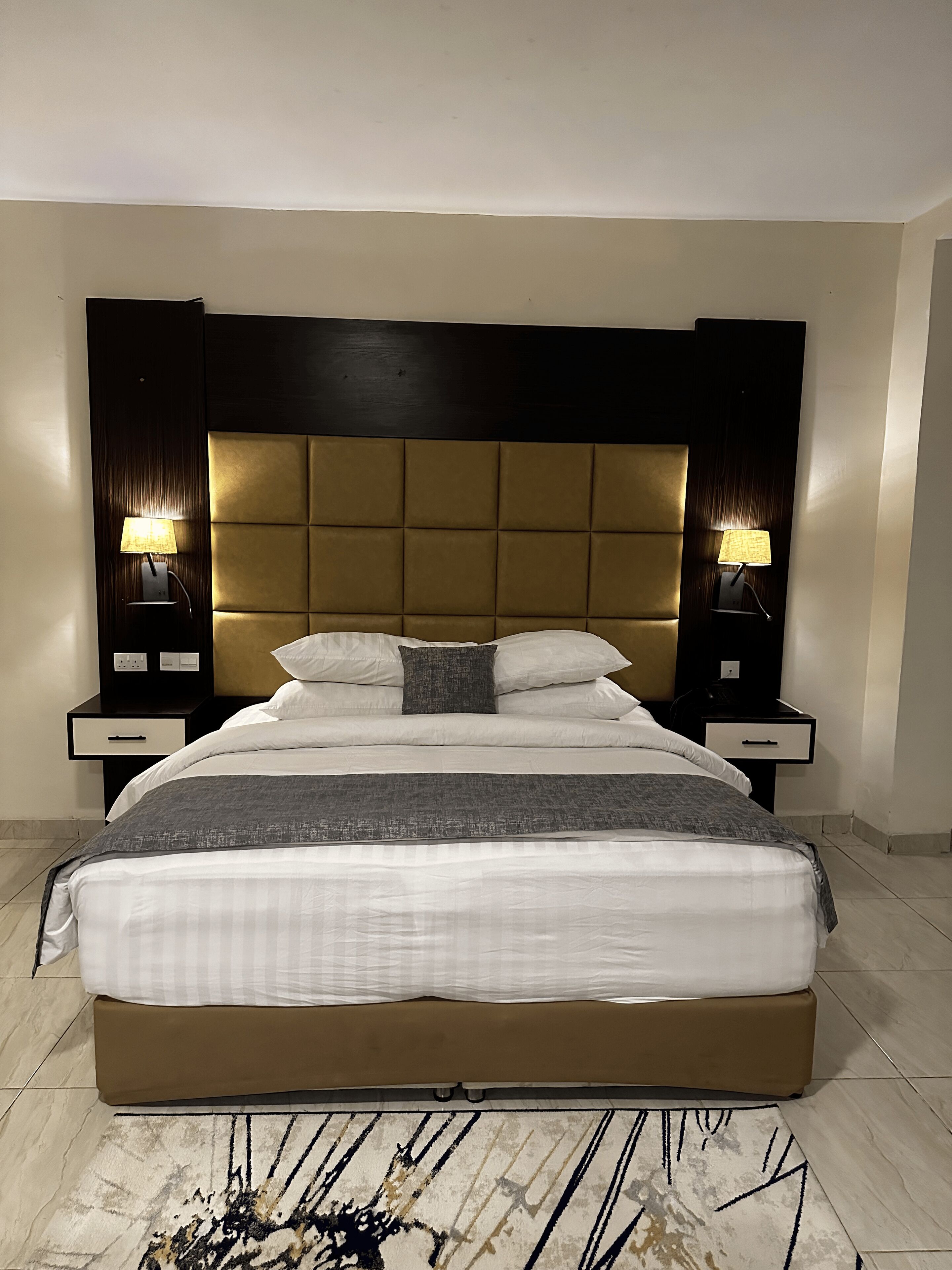 A modern hotel room with a large bed, two bedside tables, and a headboard.