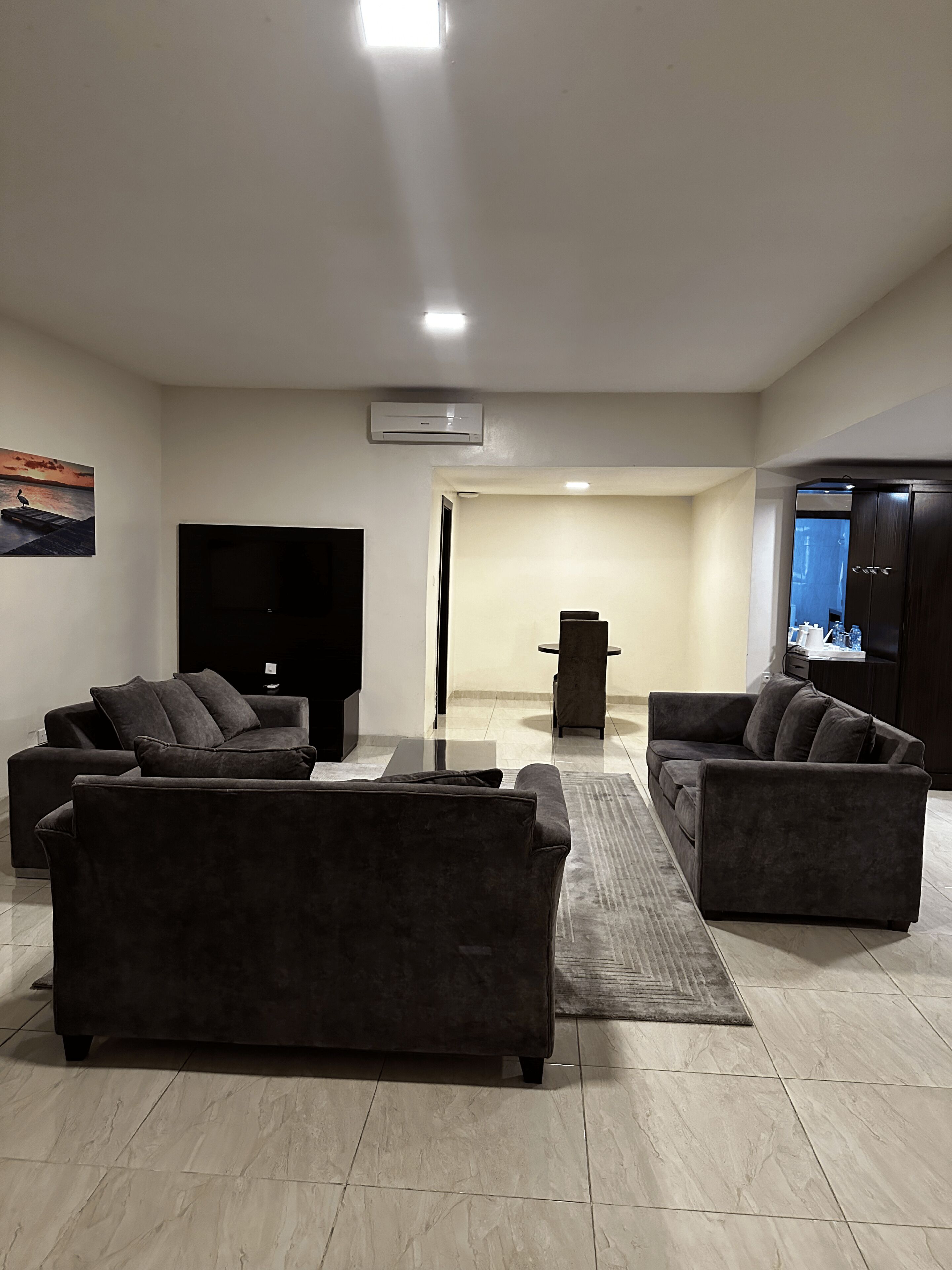 A modern living room with two dark sofas, a flat-screen TV, and a large window with a view of the water.