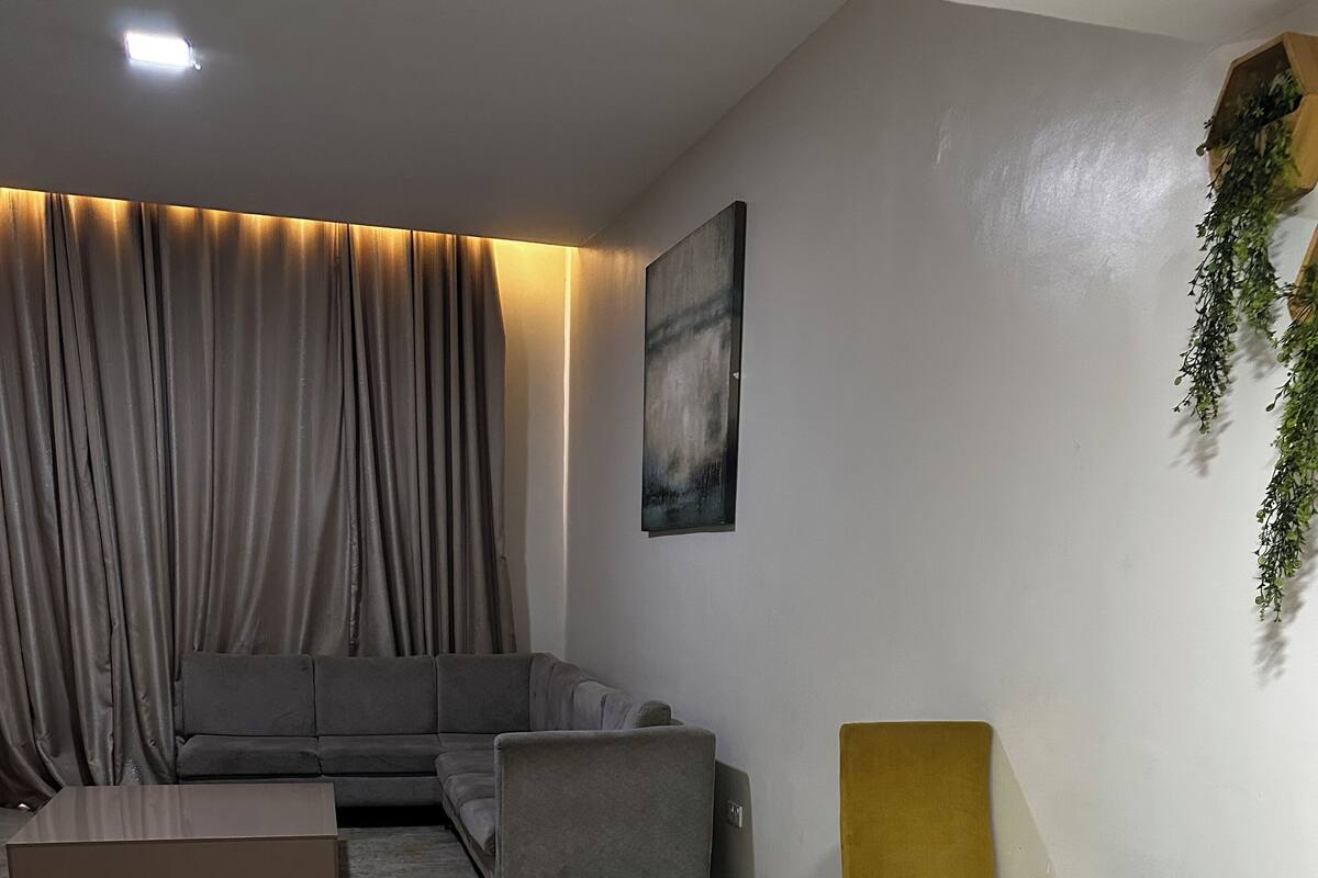 Una sala de estar moderna con un sofá, un sillón amarillo, una mesita y un ventanal con cortinas.
