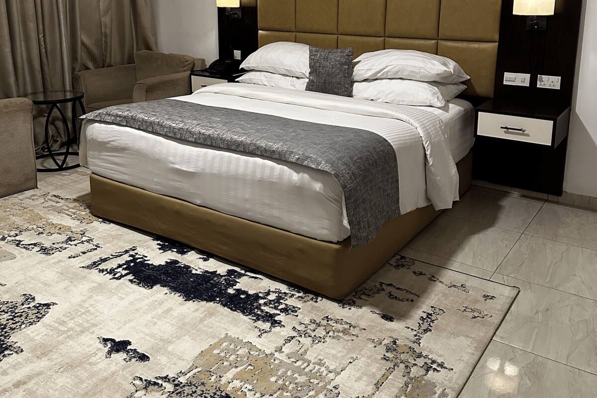 Un dormitorio moderno con una cama grande, un cabecero con iluminación integrada, una mesita de noche y una alfombra estampada.