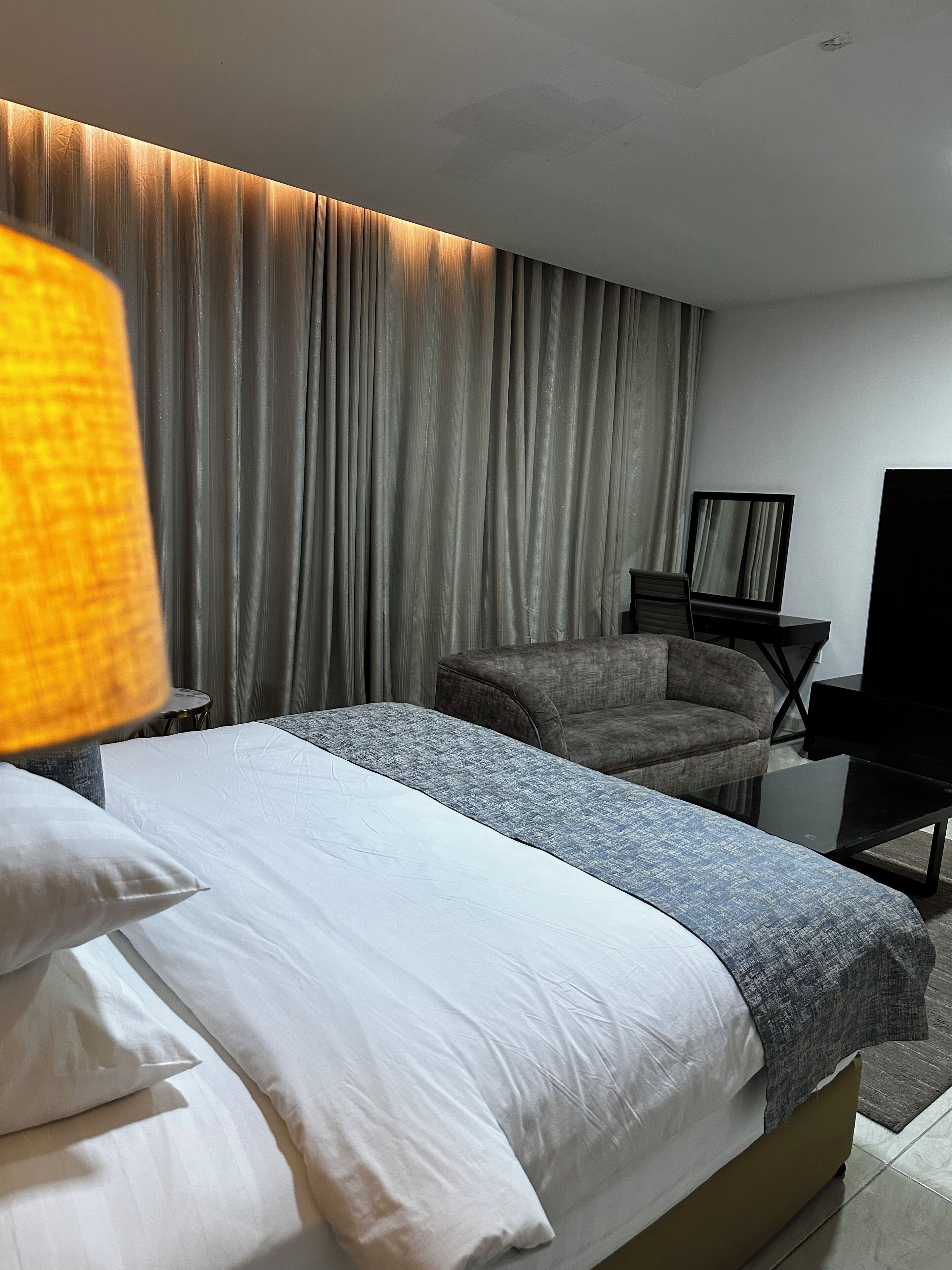 A hotel room with a bed, a sofa, a TV, and a lamp.