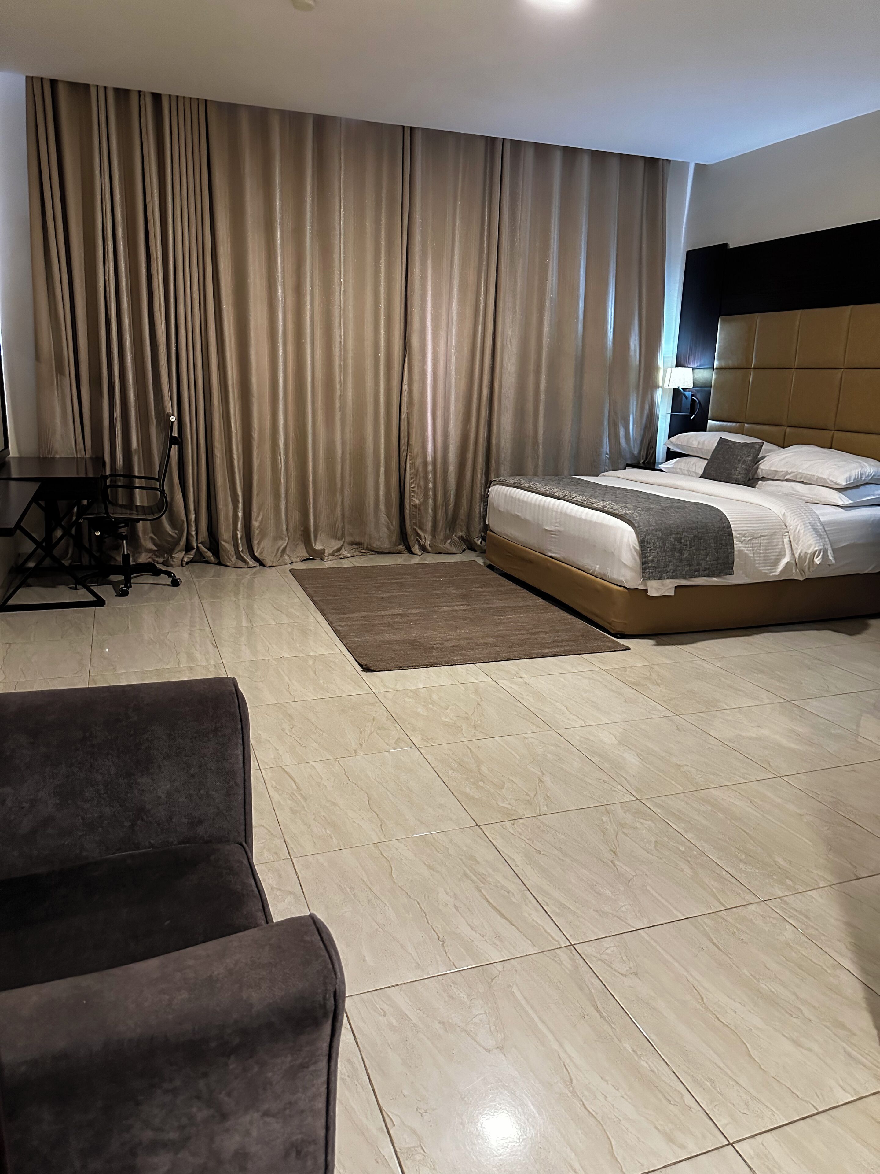 A hotel room with a bed, a desk, a chair, and a large window with curtains.