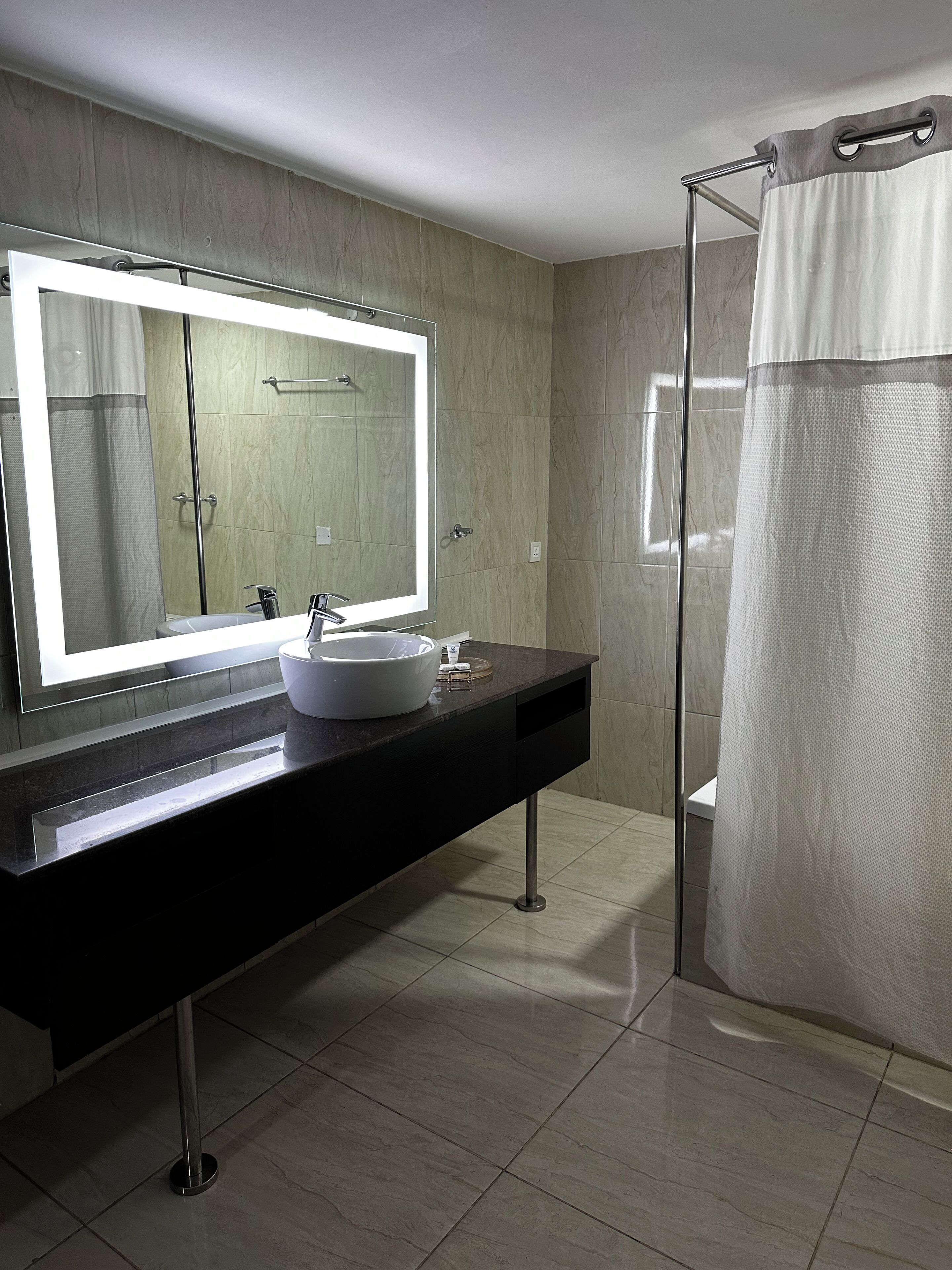 Une salle de bain moderne avec un grand miroir, un lavabo blanc et une douche à parois de verre.