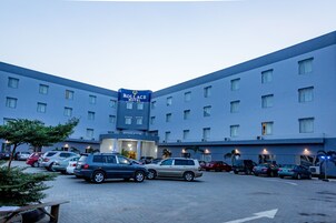 A hotel with a parking lot full of cars, a sign reading "Rollace Hotel", and a building with multiple windows.