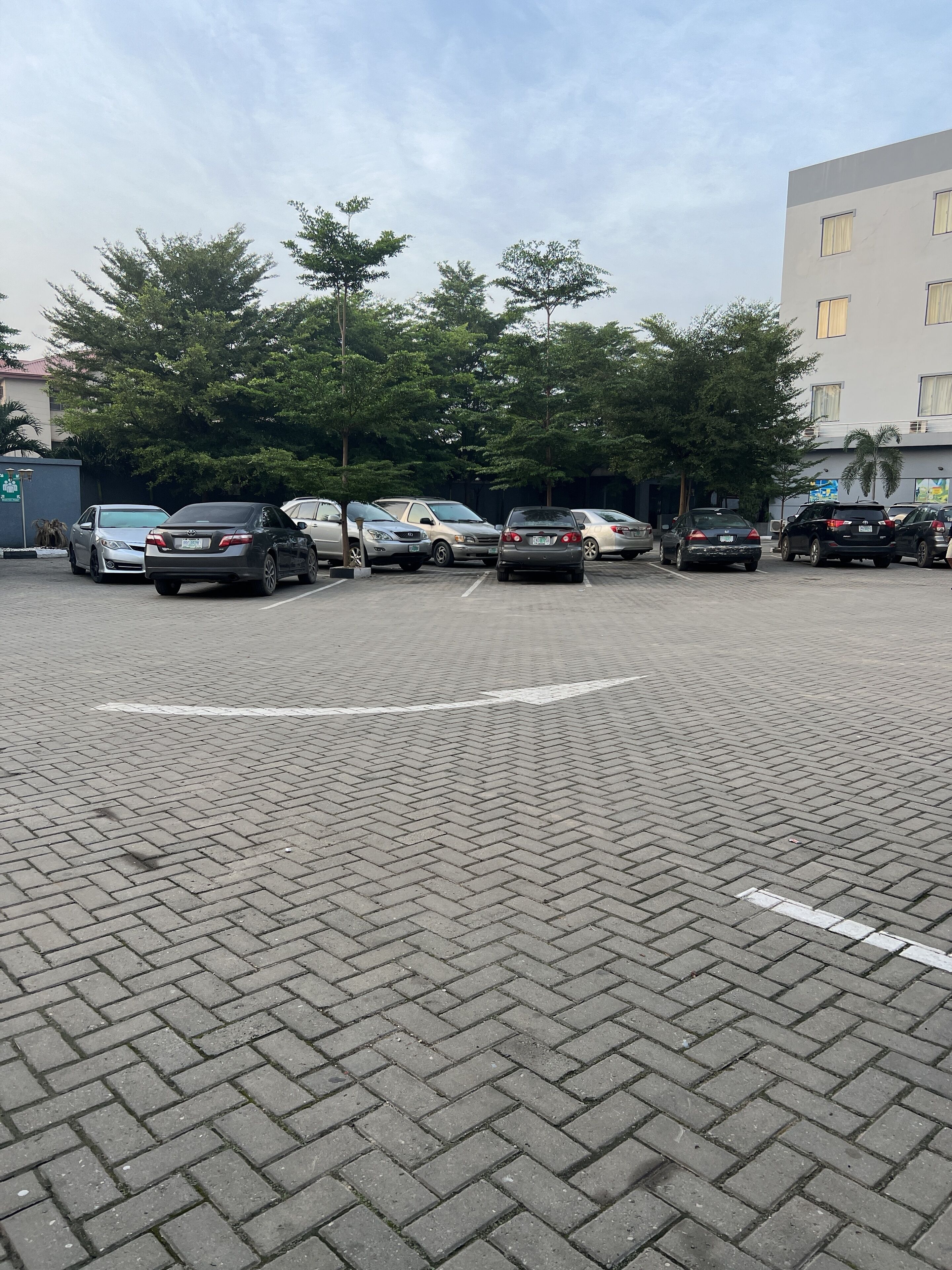 A parking lot with several cars parked in rows, surrounded by trees and buildings.