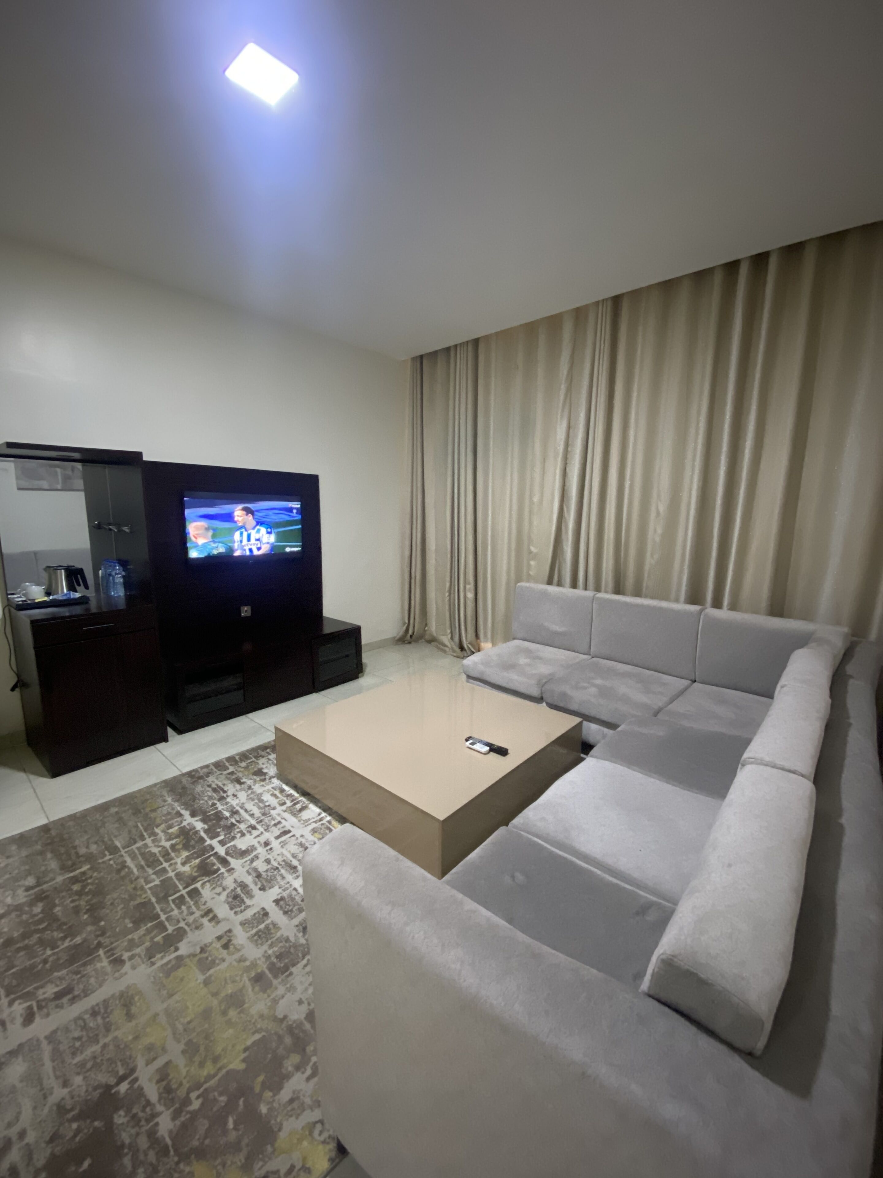 A living room with a flat-screen TV, a grey sofa, a coffee table, and a patterned rug.