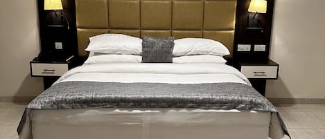 A large bed with a tufted headboard, two bedside tables with lamps, and a patterned rug.