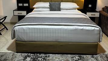 A large bed with a tufted headboard, two bedside tables with lamps, and a patterned rug.