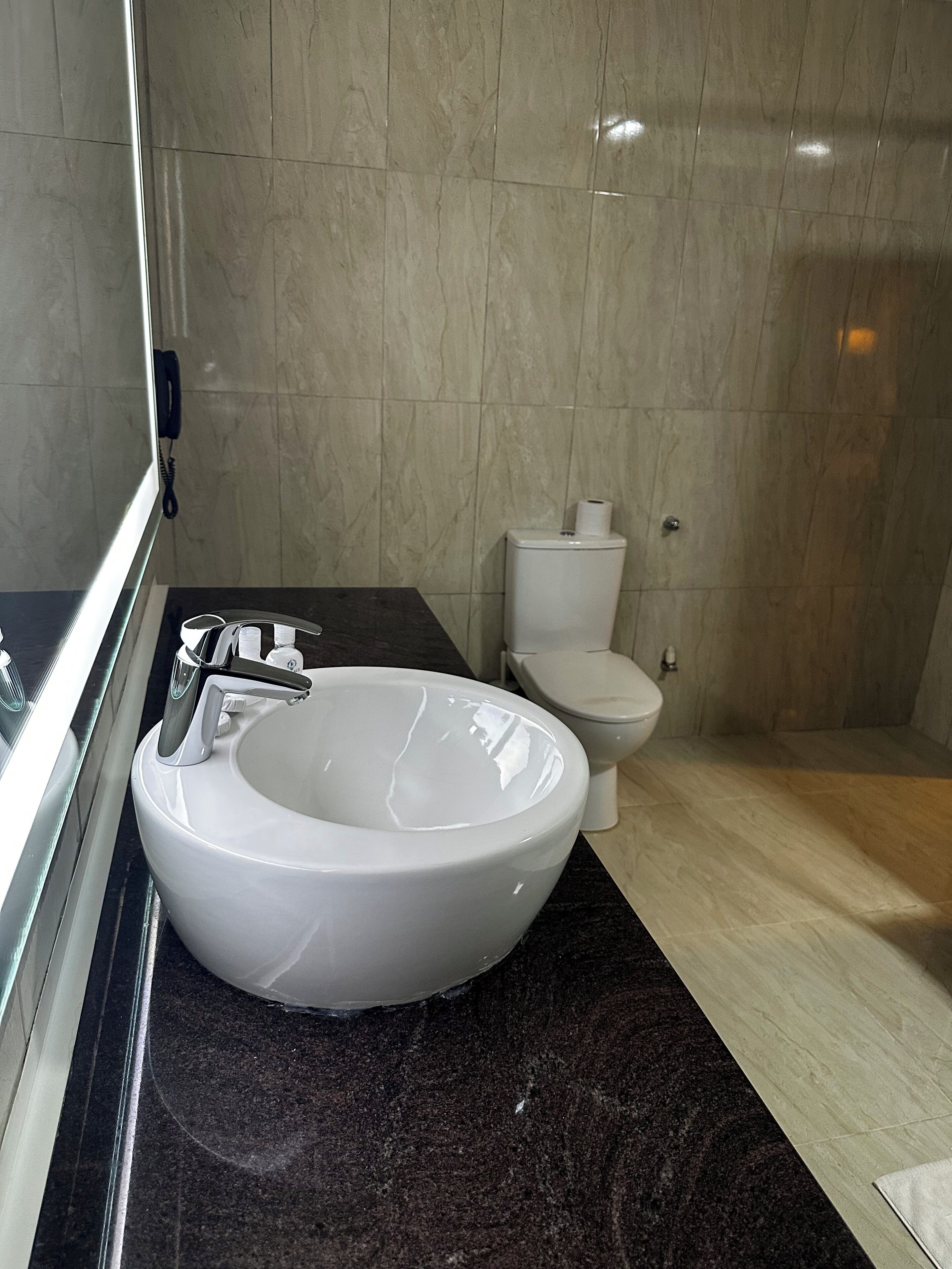 A modern bathroom with a white sink, black countertop, and a toilet.