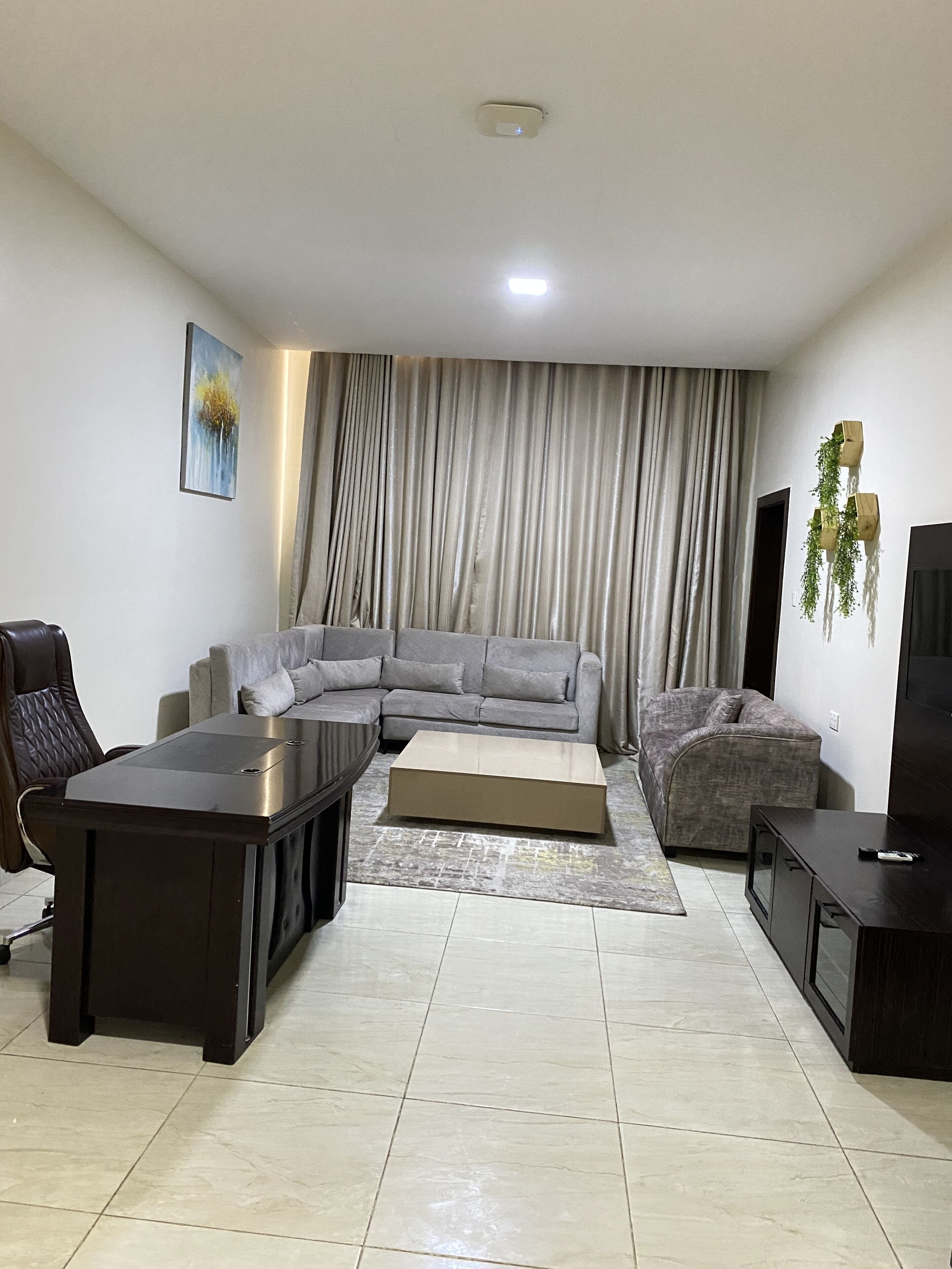 A living room with a sectional sofa, a coffee table, a TV stand, and a painting on the wall.