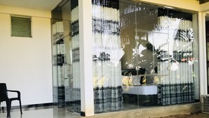 A room with a glass door, a chair, and a bed with patterned curtains. - Rivonway Hotel Polonnaruwa (Giritale)