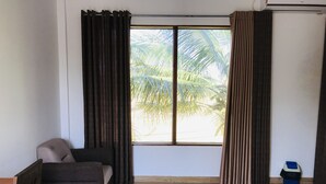 A room with a bed, a sofa, a window with curtains, and a trash bin. - Rivonway Hotel Polonnaruwa (Giritale)