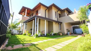 A modern two-story house with a covered patio, a well-maintained lawn, and a variety of potted plants. - Dreamvilla (Kochchikade)