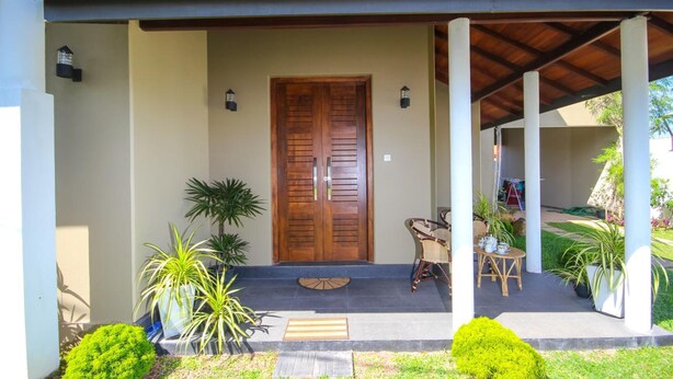 A covered porch with a wooden door, potted plants, and a small table with chairs. - Dreamvilla (Kochchikade)