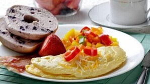 Ein Teller mit einem Omelett, Erdbeeren, Paprika und einem Bagel mit Frischkäse.