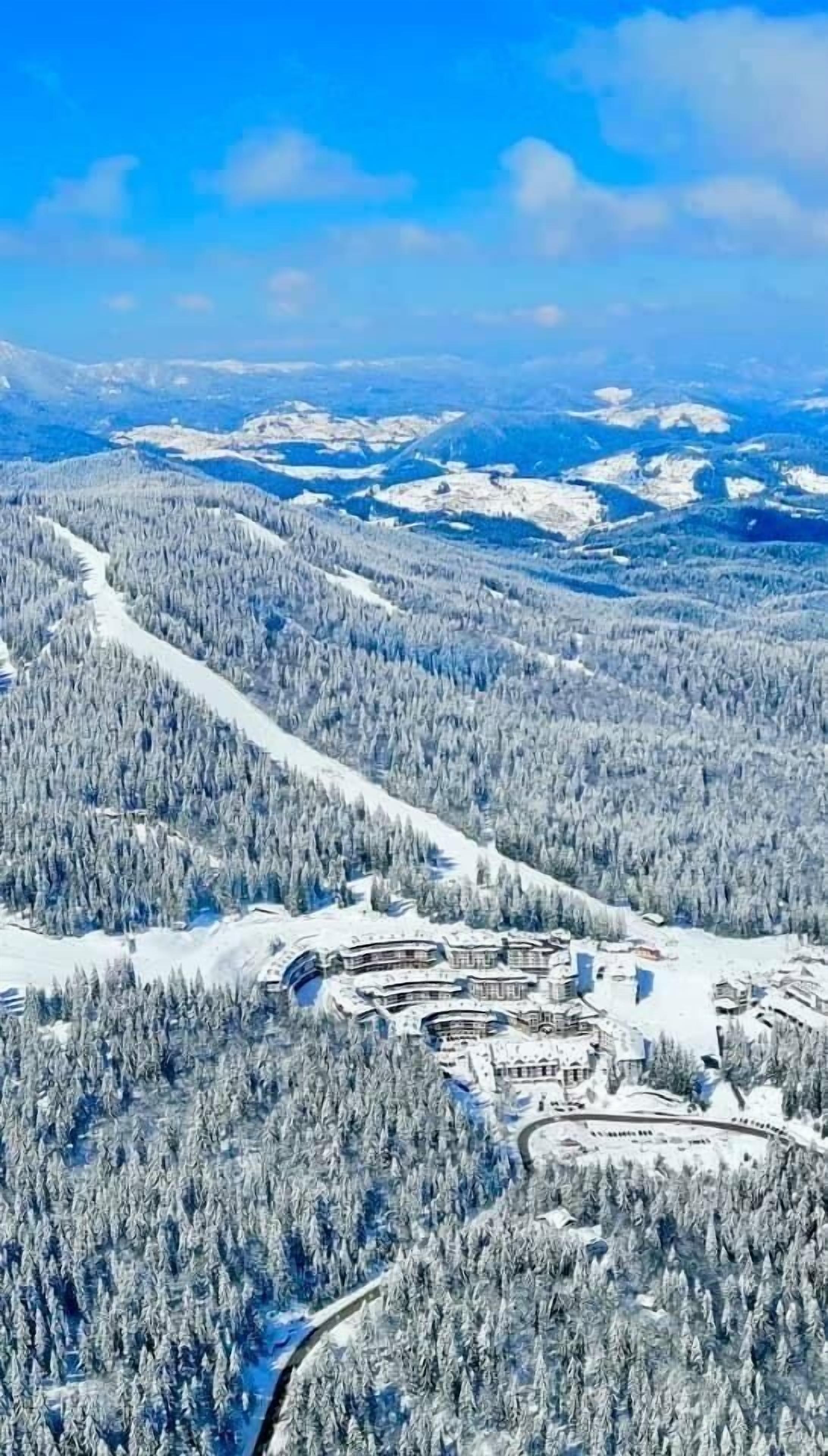 Paisagem coberta de neve com um resort de esqui, edifícios e uma estrada sinuosa.