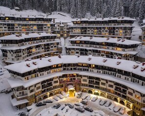 A multi-story hotel with a central courtyard, snow-covered balconies, and a parking area. - Grand Monastery Private Apartments (Smolyan)