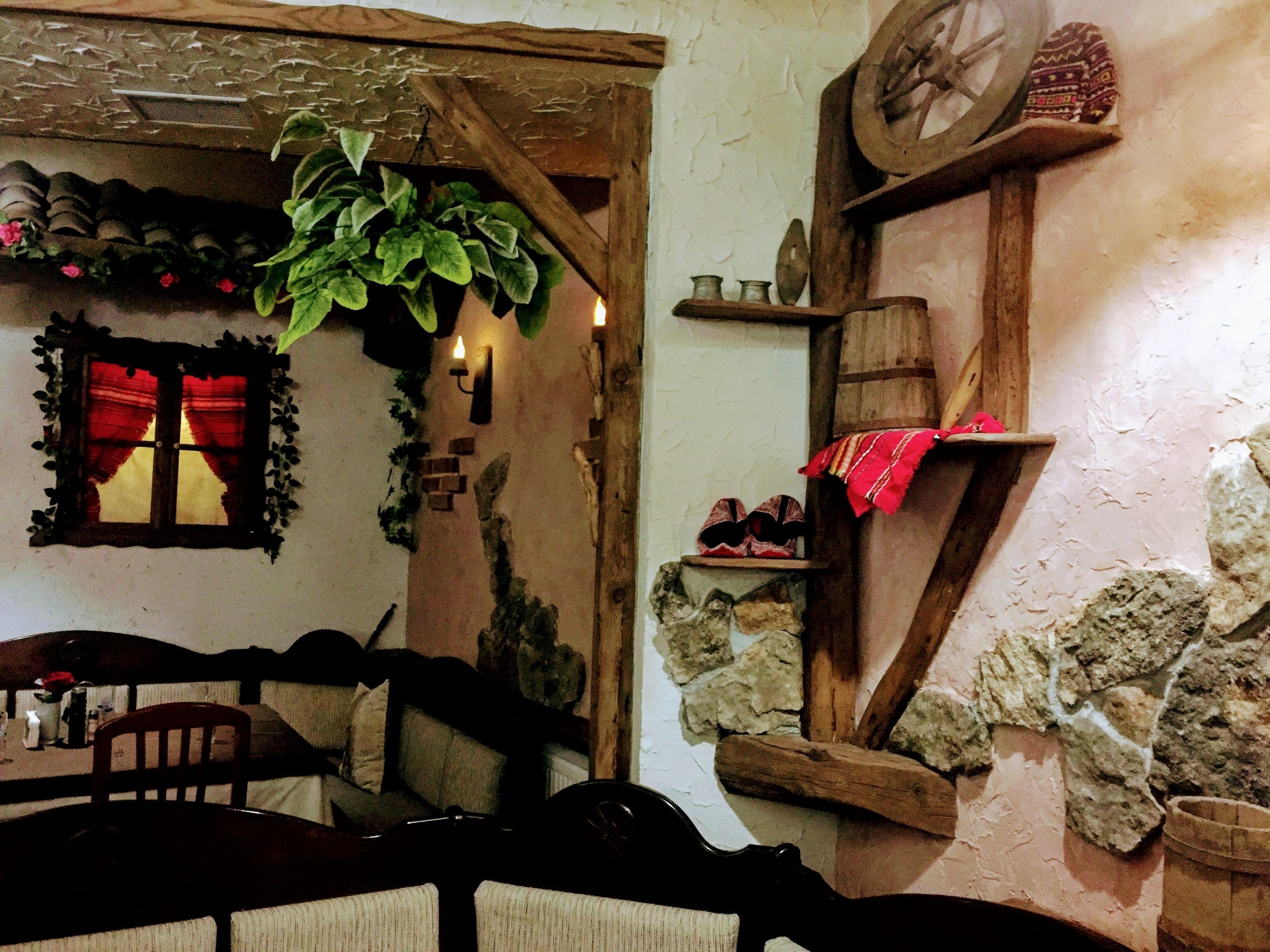 Un intérieur rustique avec une table en bois, des chaises, un mur en pierre et une fenêtre ornée de rideaux rouges.