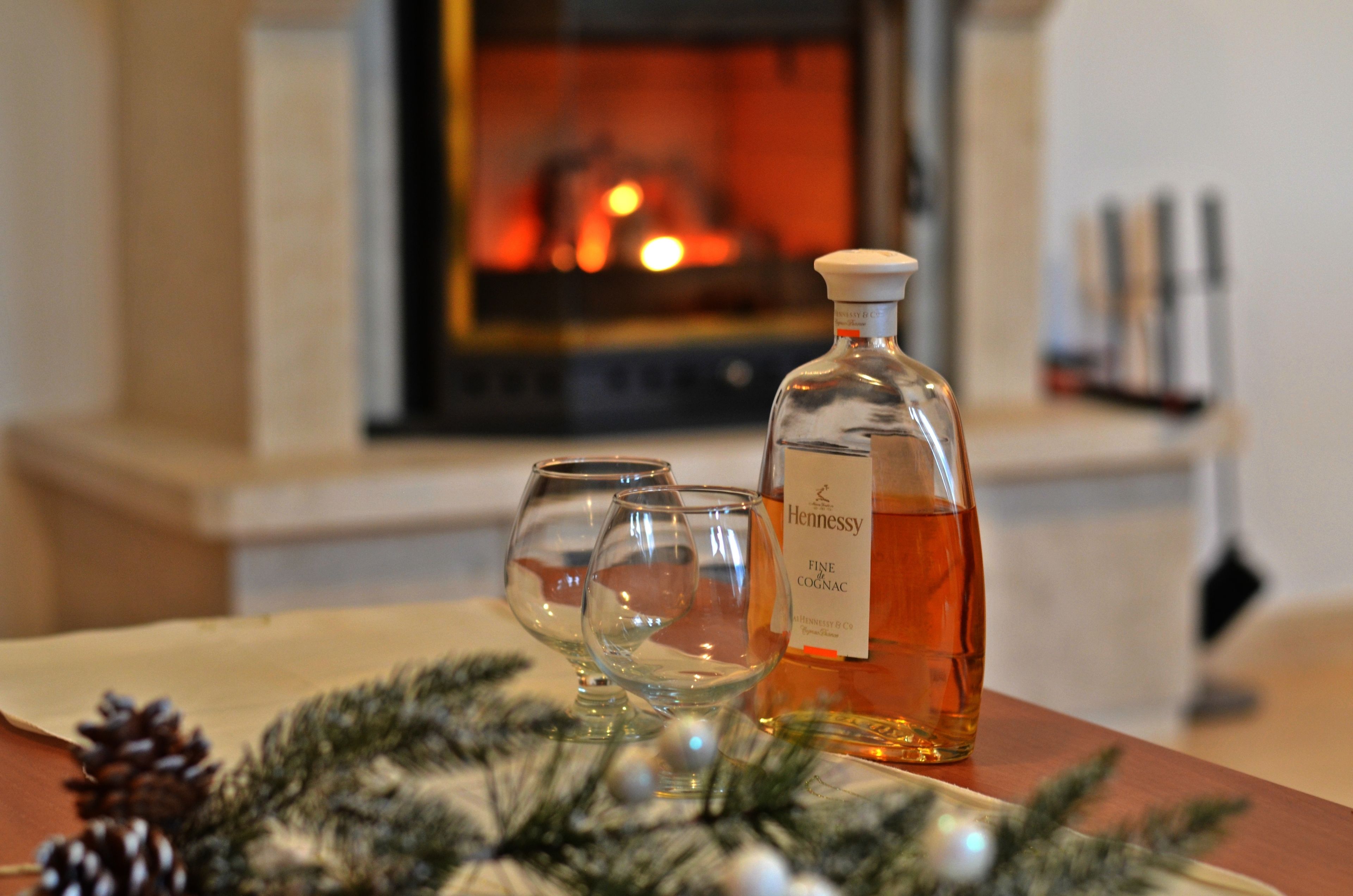 Una botella de coñac Fine Hennessy y dos vasos vacíos sobre una mesa con adorno navideño.