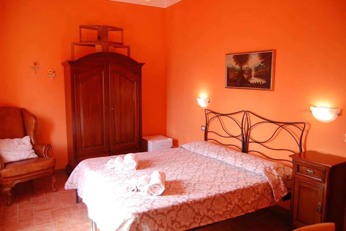 A bedroom with a bed, a wooden wardrobe, a chair, and two wall-mounted lamps.