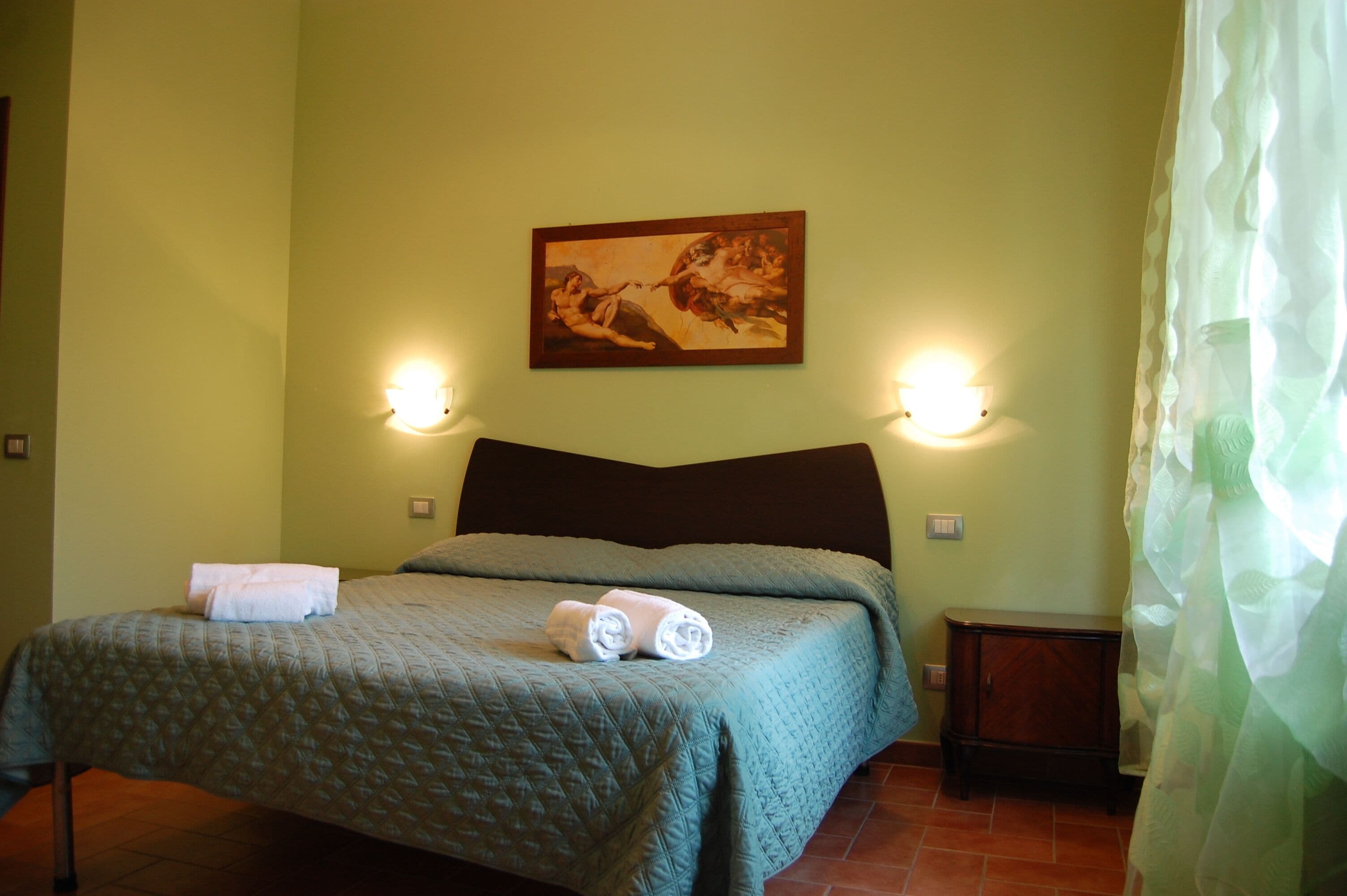 Une chambre d’hôtel avec un lit, deux lampes fixées au mur, un tableau et une table de chevet.