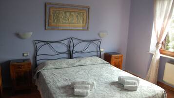A neatly made bed with a patterned bedspread and two towels on the side. There is a wall-mounted picture above the bed and two bedside tables with lamps.