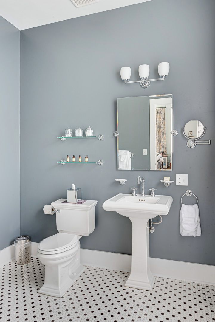 A bathroom with a toilet, sink, and mirror. There are shelves with toiletries and a towel rack.