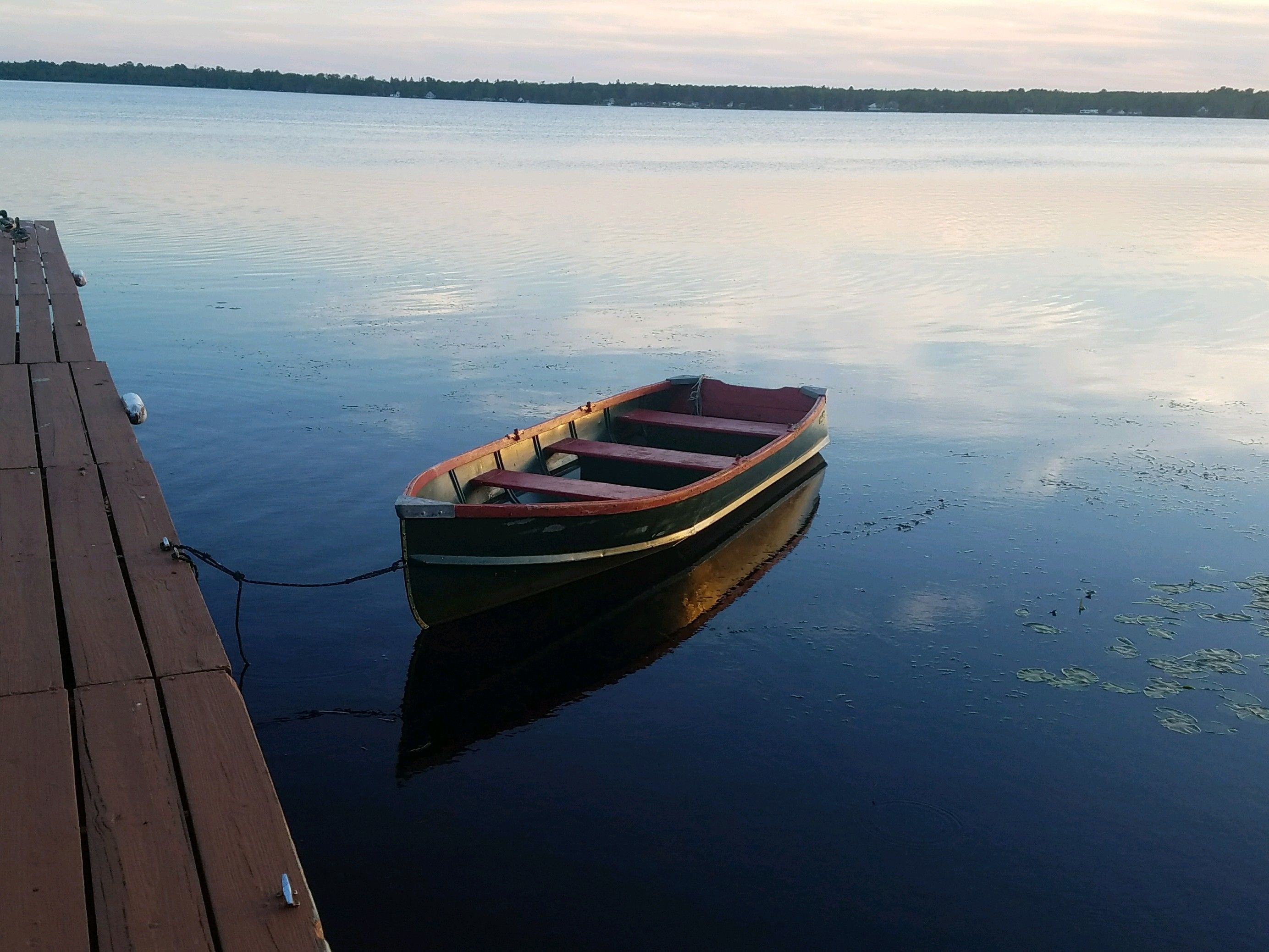 A small rowboat tied to a wooden dock extending into calm water.