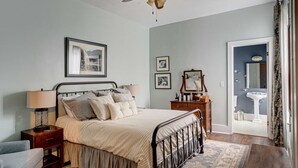 Un dormitorio con cama, mesitas de noche, ventilador de techo y vistas al baño.
