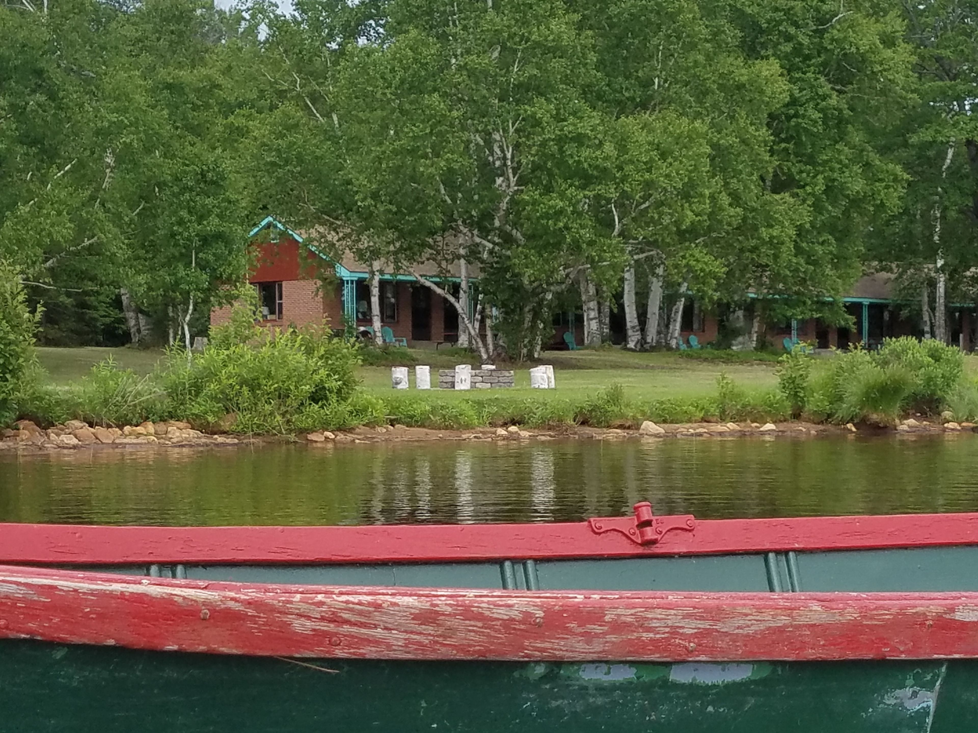 A lakeside view with a cabin, a dock, and a grassy area with chairs.