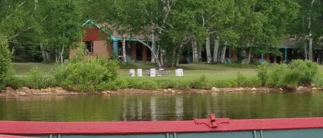 A lakeside view with a cabin, a dock, and a grassy area with chairs.
